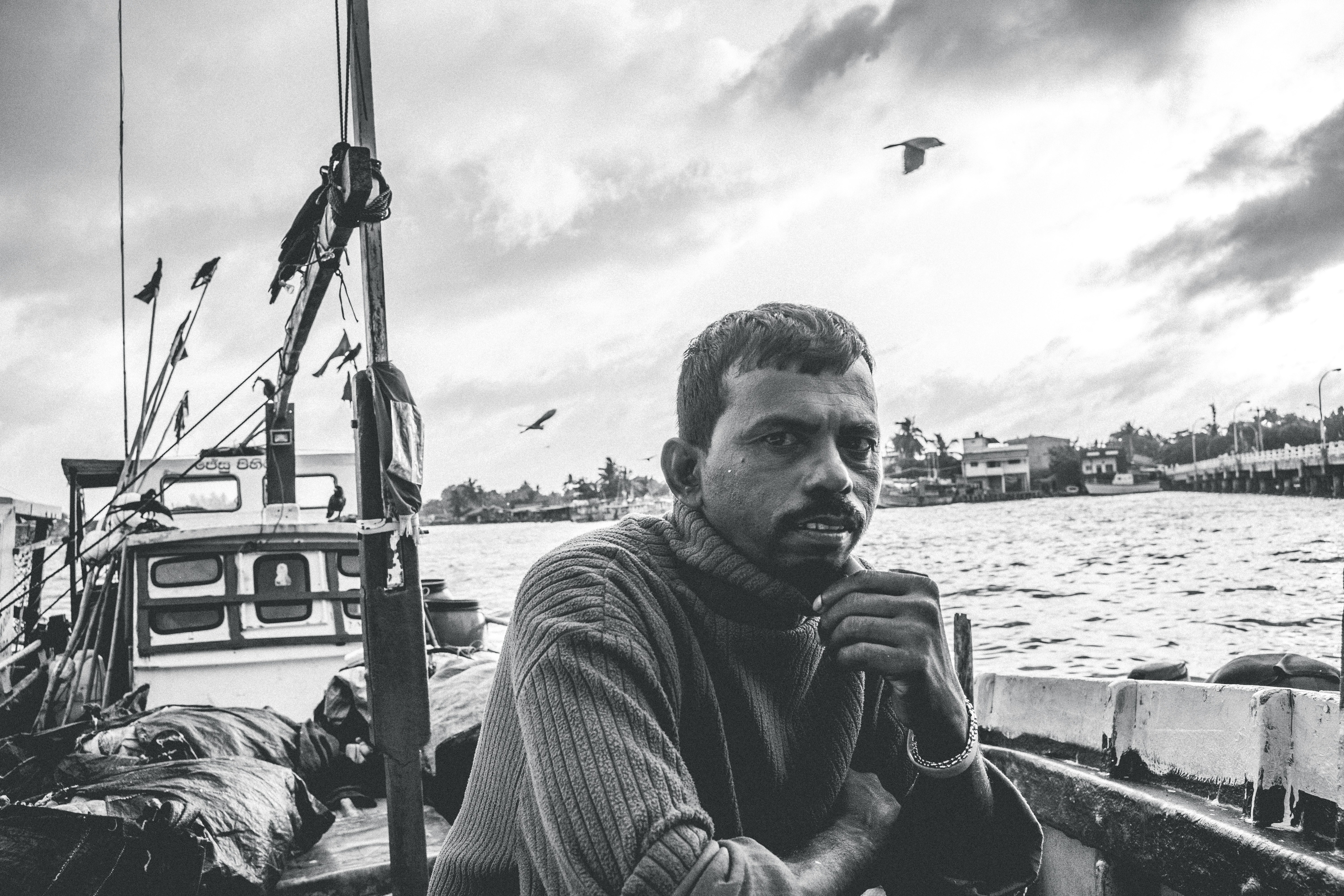 grayscale photo of man in striped shirt sitting on boat